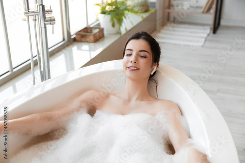Relaxed young woman with earphones taking bath at home