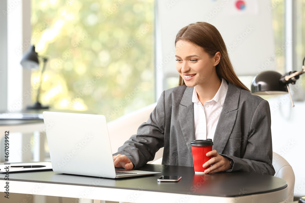 Young woman working on laptop and drinking coffee in office Young woman working on laptop and drinking coffee in office