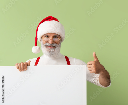 Santa Claus with blank poster showing thumb-up gesture on color background