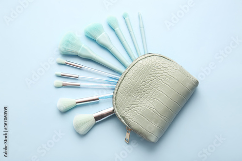 Cosmetic bag with stylish makeup brushes on blue background