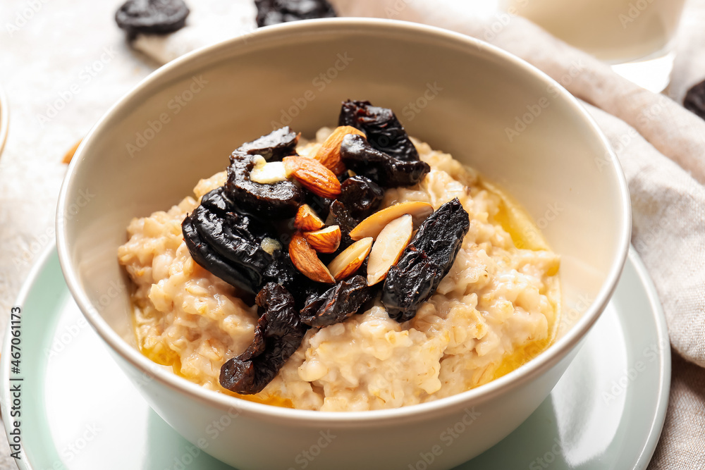 Bowl with delicious oatmeal, prunes and almond nuts on table, closeup