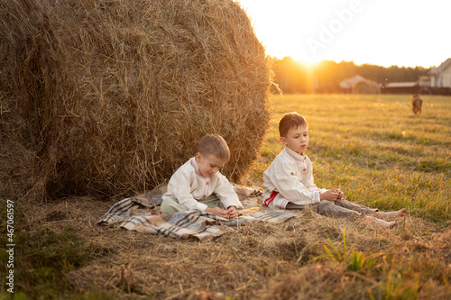 two boys sit near a haystack at sunset