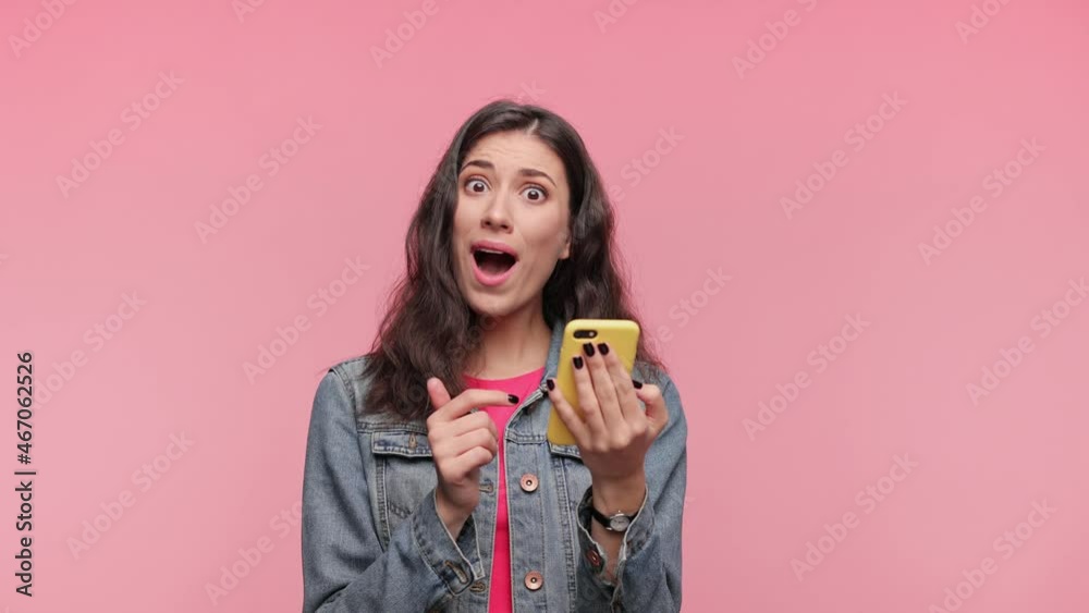Shocked smiling happy win beautiful girl 20s years in casual jacket pink t-shirt posing isolated on pink background in studio. People lifestyle concept. Look surprised wow hold using mobile cell phone Shocked smiling happy win beautiful girl 20s years in casual jacket pink t-shirt posing isolated on pink background in studio. People lifestyle concept. Look surprised wow hold using mobile cell phone