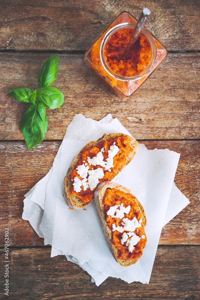 Wholegrain bread covered with tomato-pepper dip and feta cheese over old rustic wooden table. Homemade organic vegetable dish.