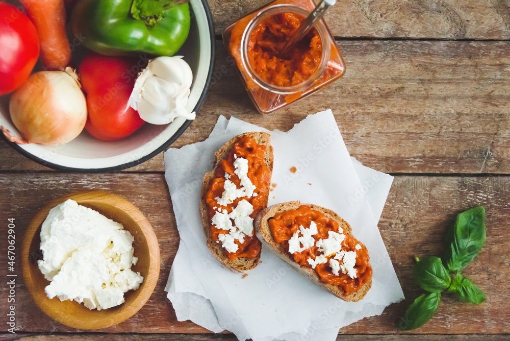 Wholegrain bread covered with tomato-pepper dip and feta cheese over old rustic wooden table. Homemade organic vegetable dish.