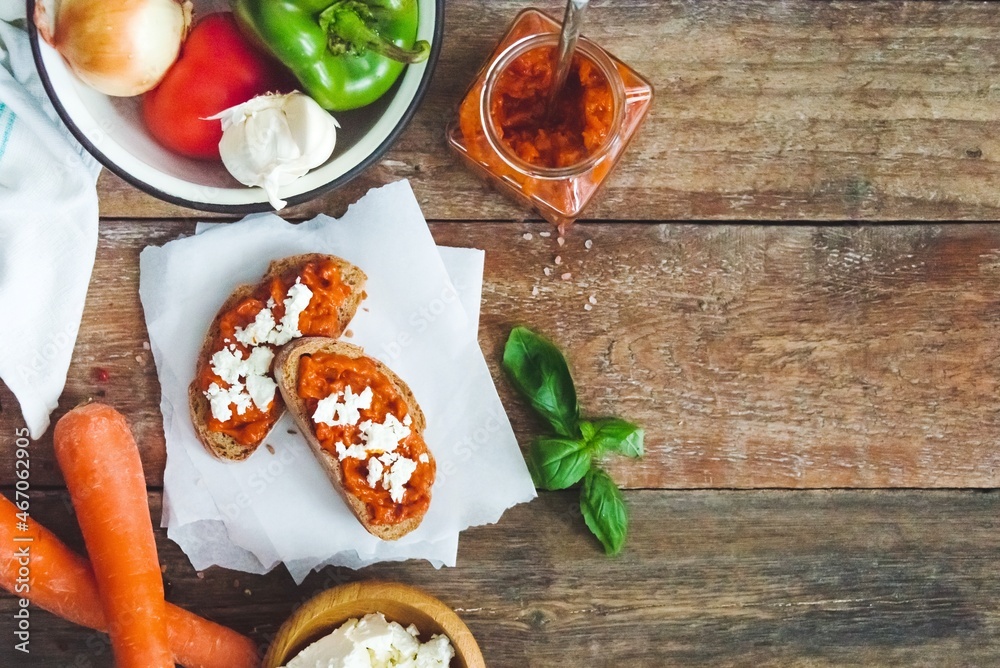 Wholegrain bread covered with tomato-pepper dip and feta cheese over old rustic wooden table. Homemade organic vegetable dish.