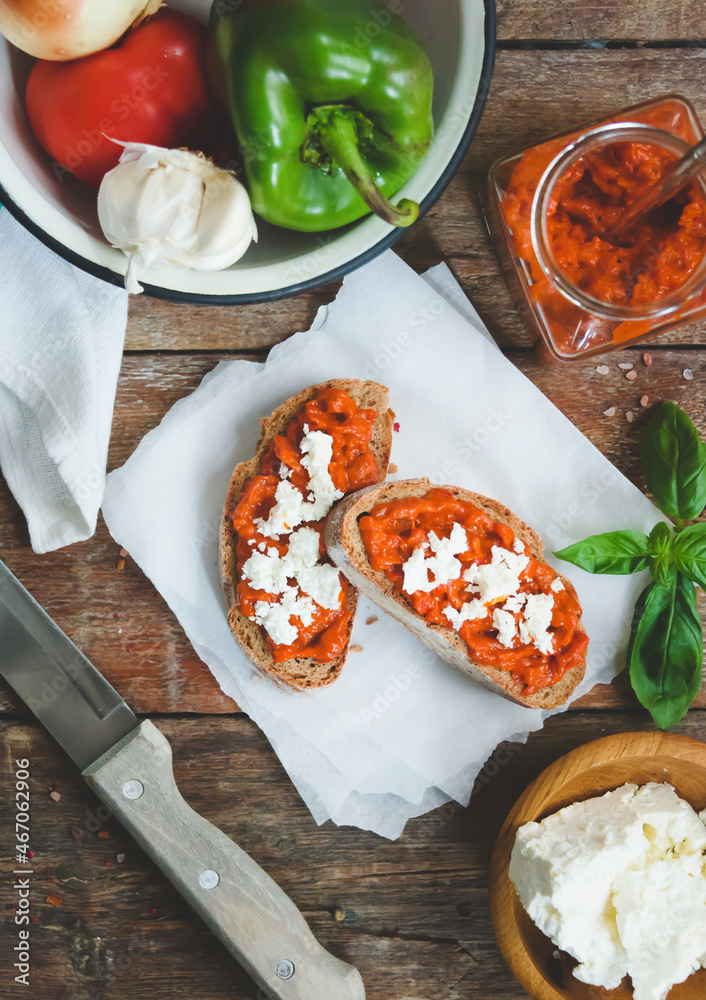 Wholegrain bread covered with tomato-pepper dip and feta cheese over old rustic wooden table. Homemade organic vegetable dish.