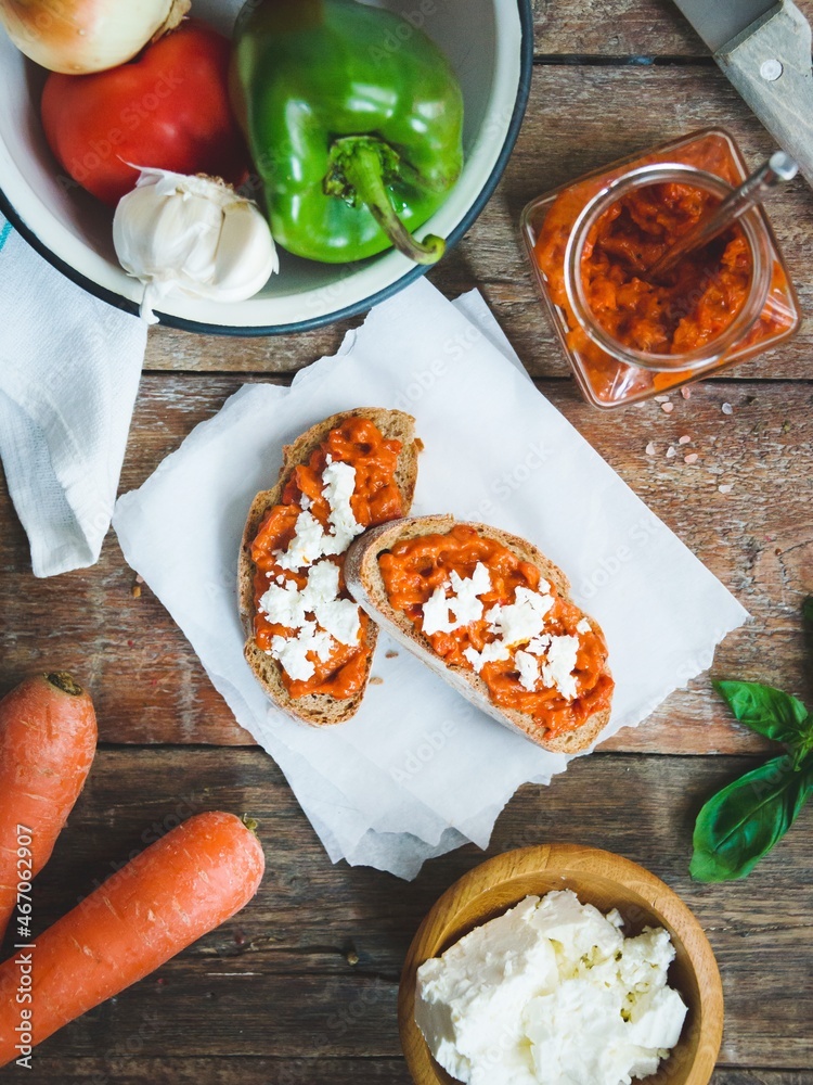 Wholegrain bread covered with tomato-pepper dip and feta cheese over old rustic wooden table. Homemade organic vegetable dish.