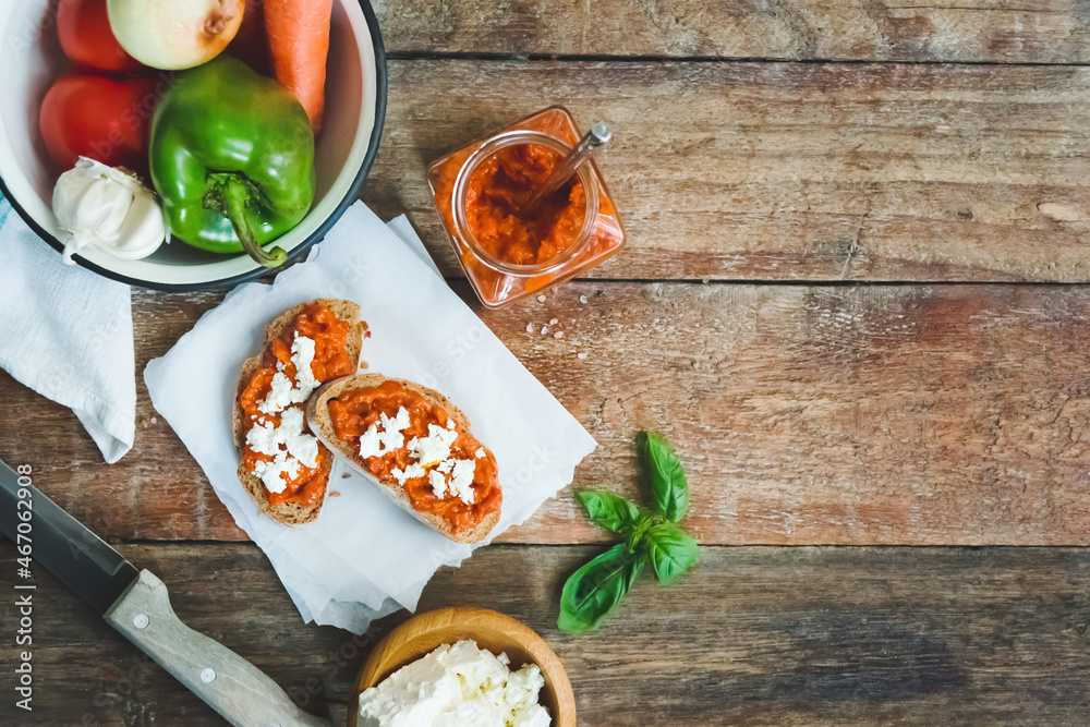 Wholegrain bread covered with tomato-pepper dip and feta cheese over old rustic wooden table. Homemade organic vegetable dish.