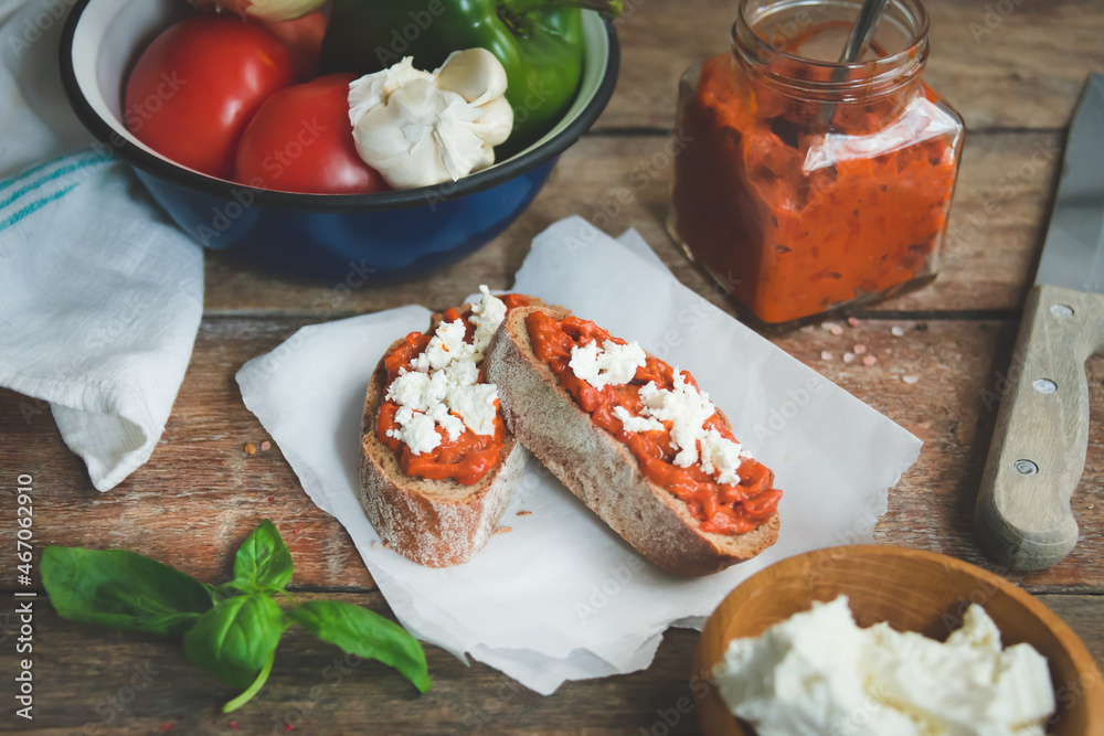 Wholegrain bread covered with tomato-pepper dip and feta cheese over old rustic wooden table. Homemade organic vegetable dish.