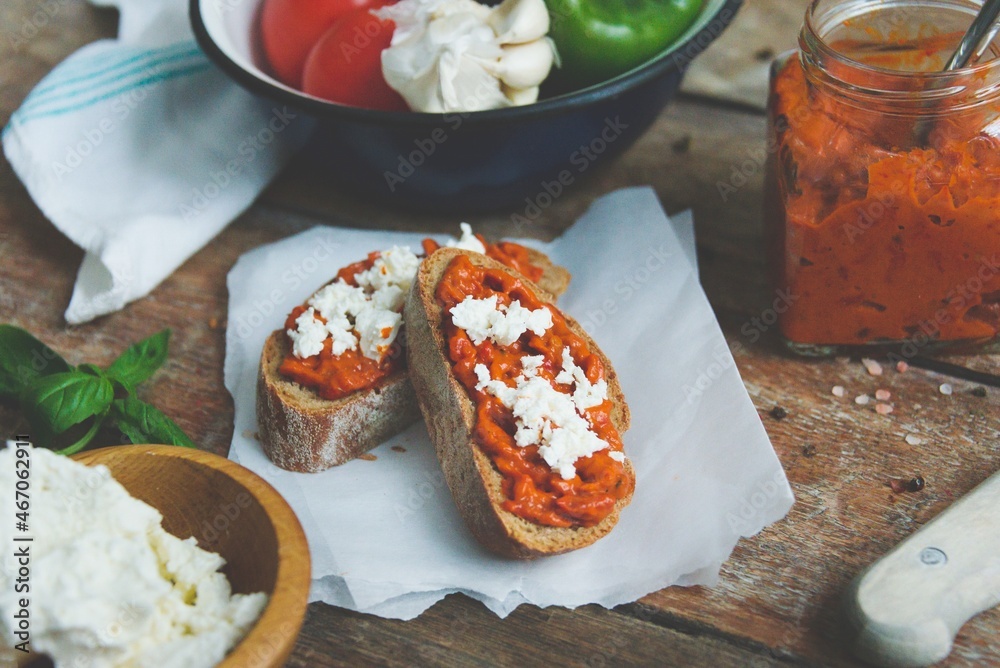 Wholegrain bread covered with tomato-pepper dip and feta cheese over old rustic wooden table. Homemade organic vegetable dish.