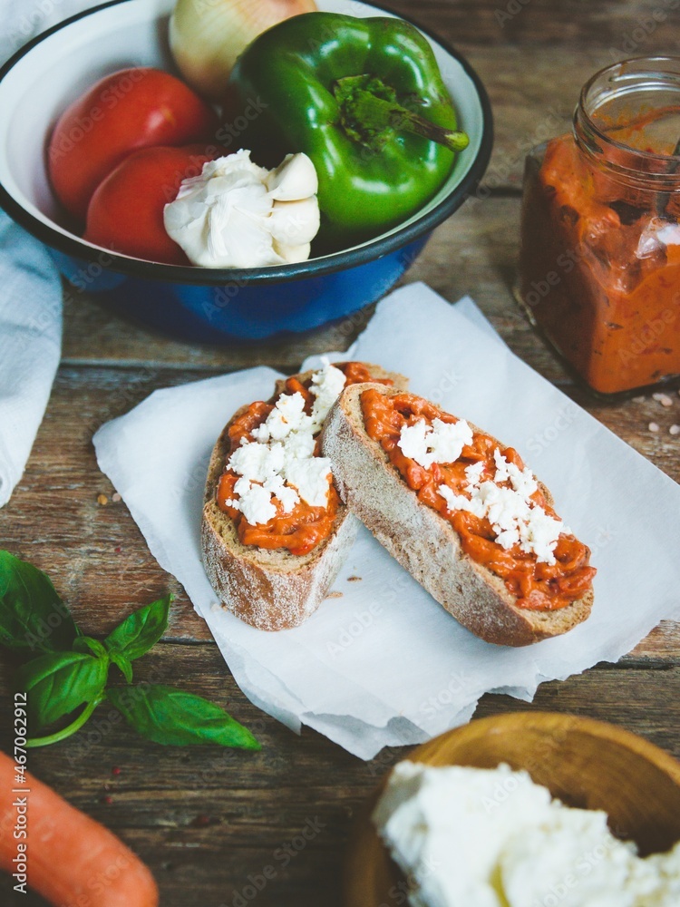 Wholegrain bread covered with tomato-pepper dip and feta cheese over old rustic wooden table. Homemade organic vegetable dish.