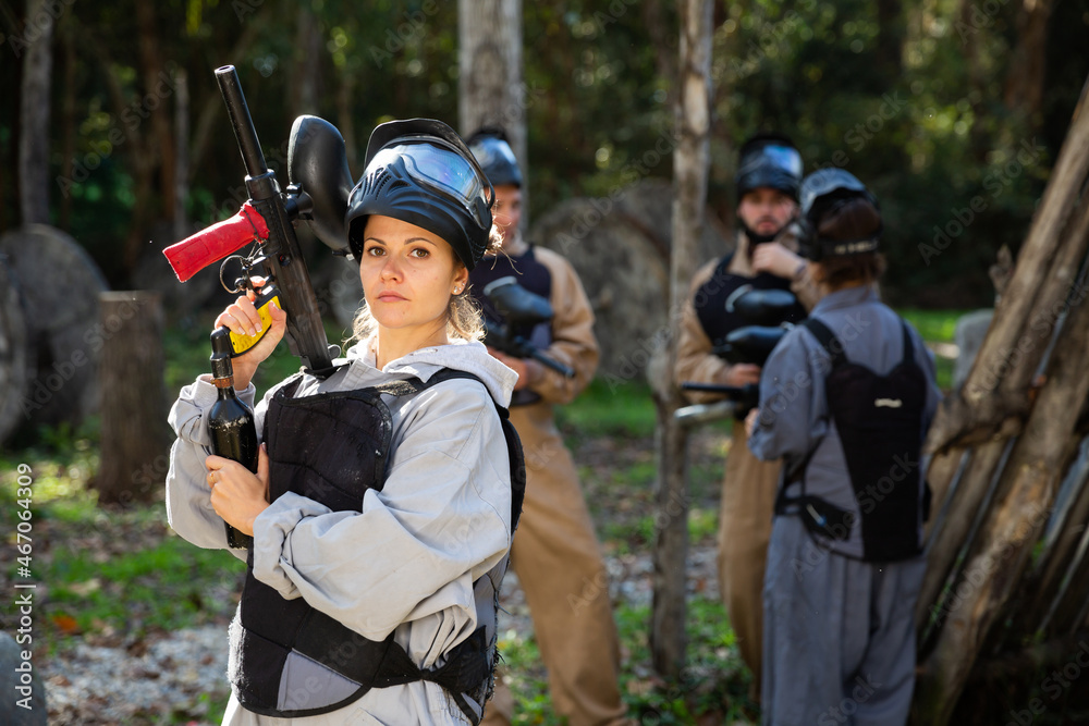 Fototapeta premium Young woman wearing uniform and holding gun ready for playing with friends on paintball outdoor