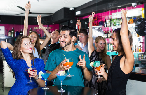 Women with man are drinking cocktails and having fun in bar