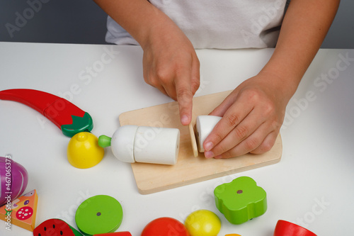 The child plays with wooden colorful toys. The child is cutting a wooden  fruit salad. Educational logic toys for kid's. Children's hands close-up. Montessori Games for Child Development