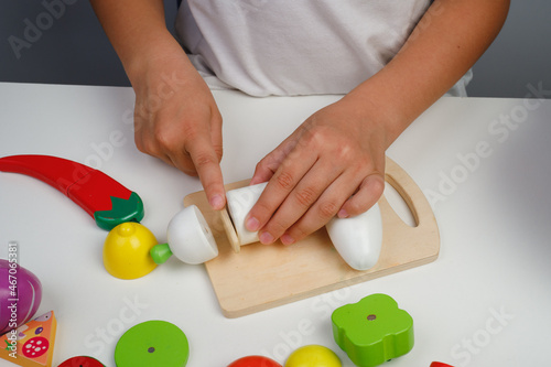 The child plays with wooden colorful toys. The child is cutting a wooden fruit salad. Educational logic toys for kid's. Children's hands close-up. Montessori Games for Child Development