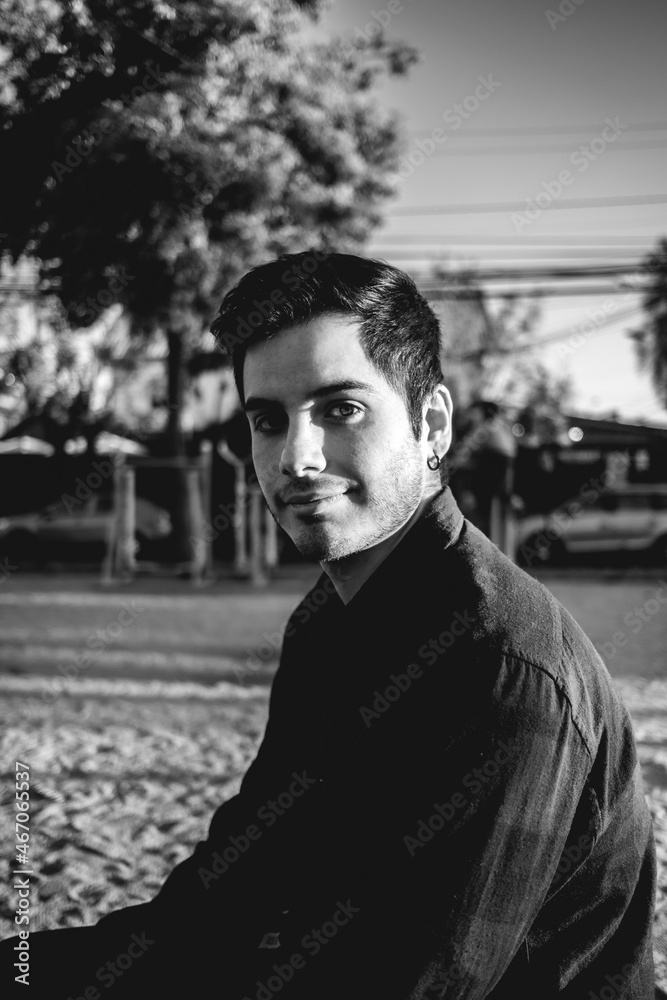 Obraz premium Handsome, young and happy caucasian guy smiling in a park in the afternoon with the sunset light in the face (in black and white)