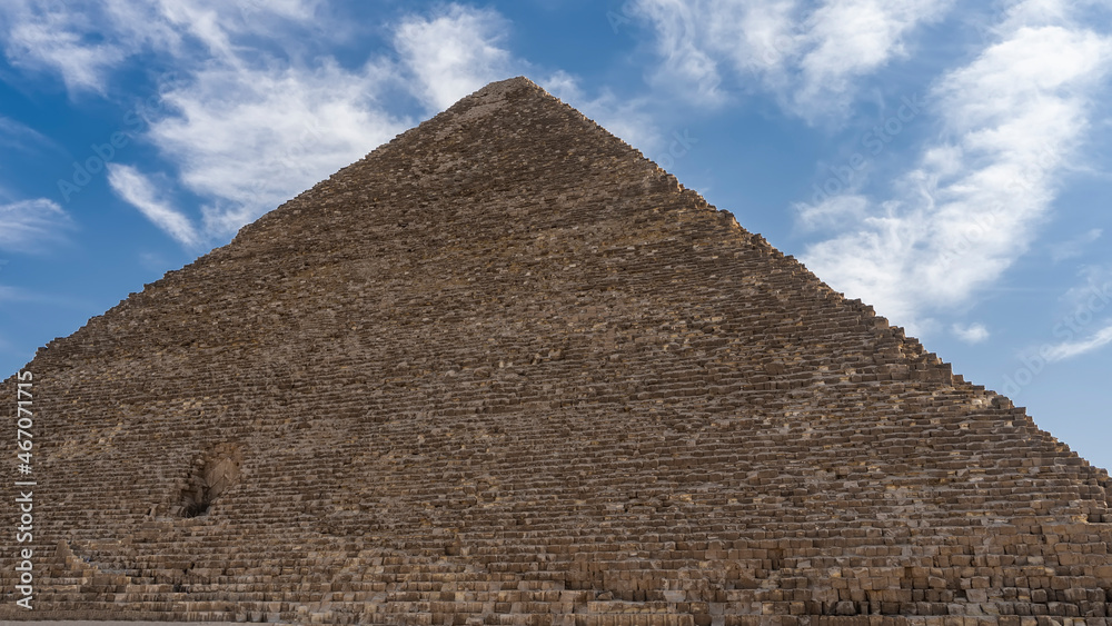 The Great Pyramid of Cheops on the background of a blue sky with picturesque clouds. On the wall, made of ancient boulders, you can see the entrance inside. Egypt. Giza