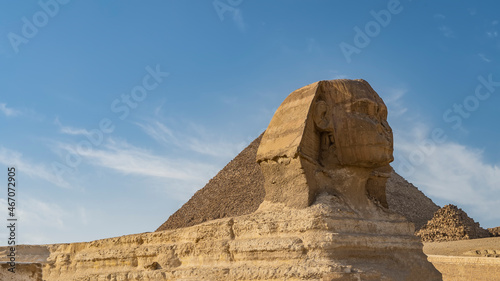 The mysterious sculpture of the Great Sphinx is carved out of stone. Profile view. In the background is an ancient pyramid  blue sky with clouds. Egypt. Giza