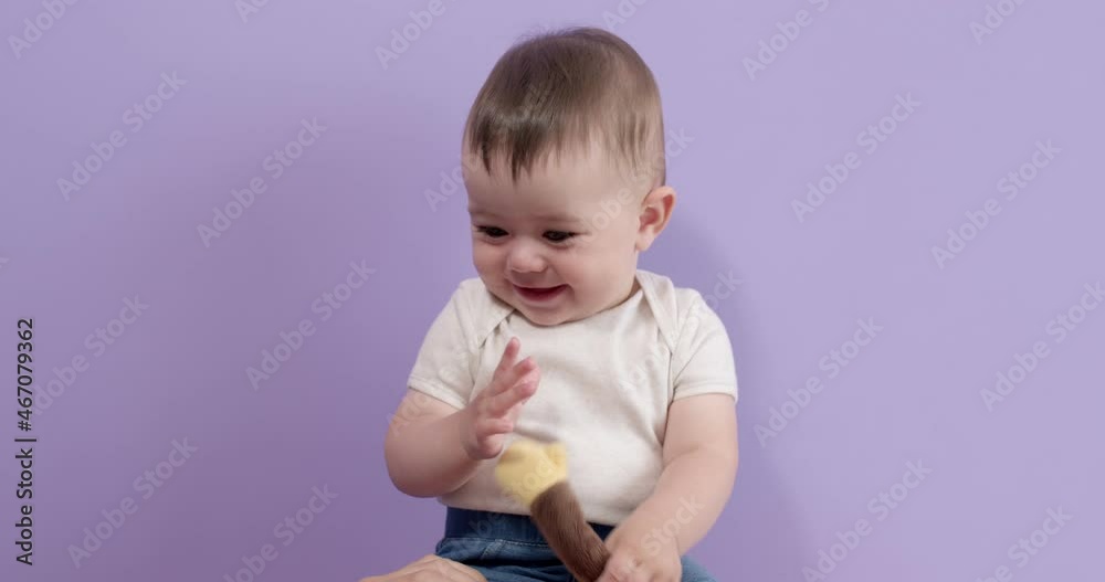 Hiney sweet little baby girl sit playing with toy in studio, isolated on purple background, having fun, innocent and infant caucasian kid toddler in casual wear is looking positive and joyous. Hiney sweet little baby girl sit playing with toy in studio, isolated on purple background, having fun, innocent and infant caucasian kid toddler in casual wear is looking positive and joyous.