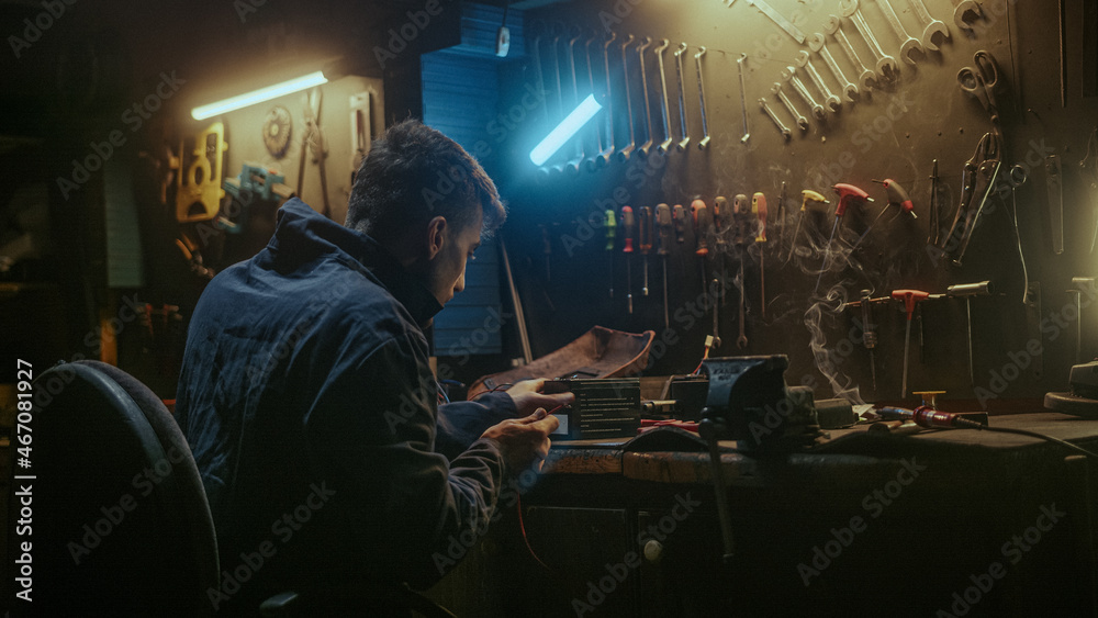 Young blacksmith man with workwear, taking solder tool, sitting on chair and do solder.