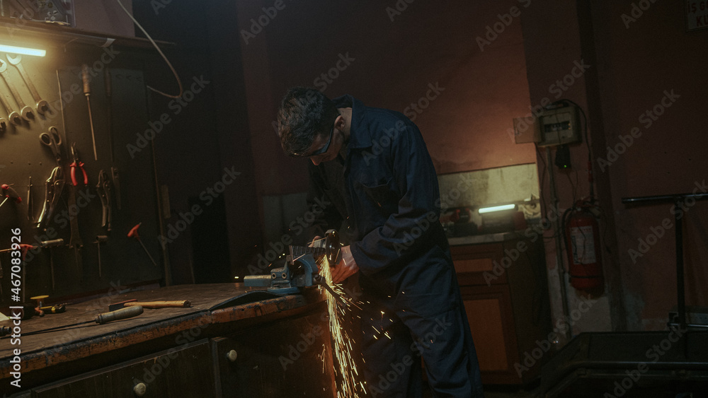 Young blacksmith man use iron or metal cutting machine and he metal grinding on steel spare part in workshop Young blacksmith man use iron or metal cutting machine and he metal grinding on steel spare part in workshop