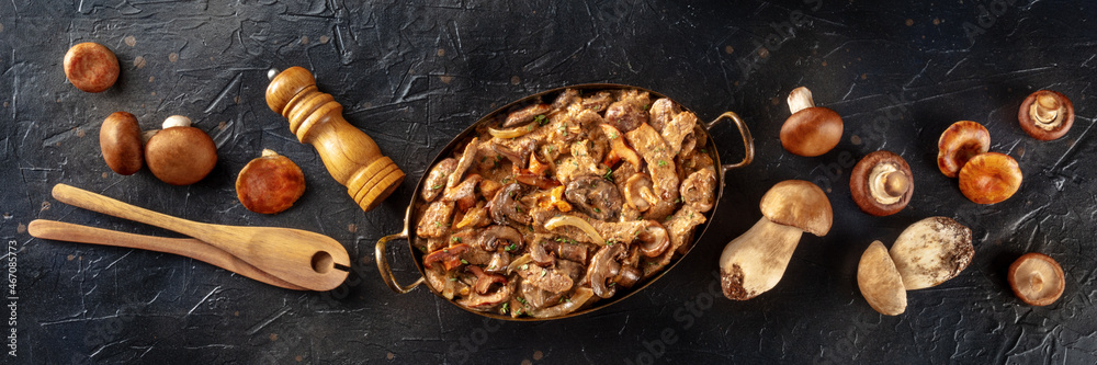 Beef stroganoff panorama. Mushroom and meat ragout with cream sauce, in a pan with ingredients, overhead flat lay shot on a black slate background Beef stroganoff panorama. Mushroom and meat ragout with cream sauce, in a pan with ingredients, overhead flat lay shot on a black slate background
