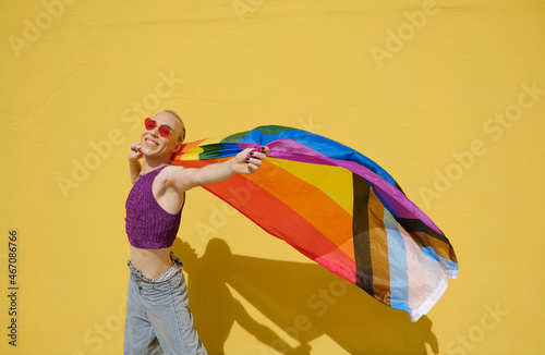 Young stylish non-binary person carrying the lgbt rainbow flag against a yellow wall. photo