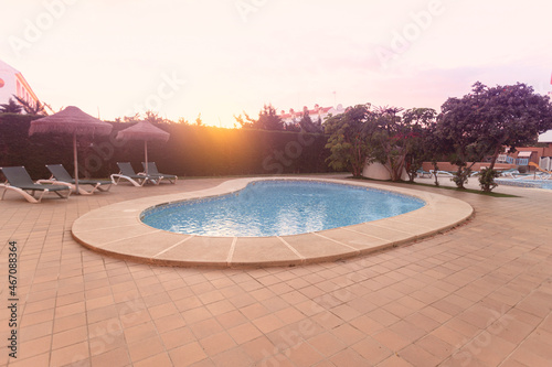 Photography of deck chair and umbrella and a pool  a residential area during the sunset with palms and pool