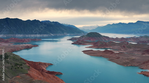 Aerial flight Beautiful spring landscape of river with blue turquoise water and hills against background of mountains and dawn sky. Bare rocky shores are visible due to ow water level on the lake.