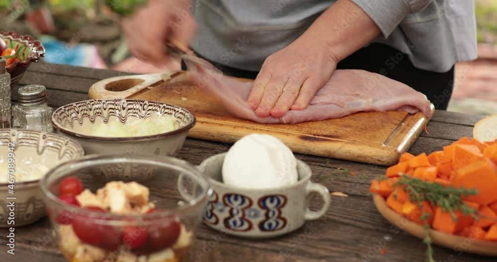 Female hands cut turkey fillet with knife, then tenderize meat by beating with meat tenderizer. Cooking of fresh raw turkey breast on wooden cutting board at rustic table with traditional crockery Female hands cut turkey fillet with knife, then tenderize meat by beating with meat tenderizer. Cooking of fresh raw turkey breast on wooden cutting board at rustic table with traditional crockery