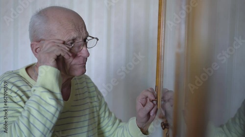 Aged bald man in glasses opening bookcase glass door and looking at books for reading. Wisdom and knowledge concept. photo