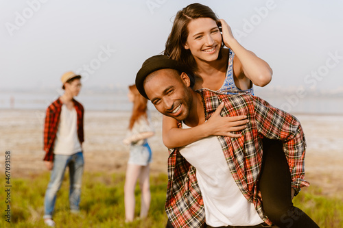 Young multiracial couple piggybacking while resting with their friends