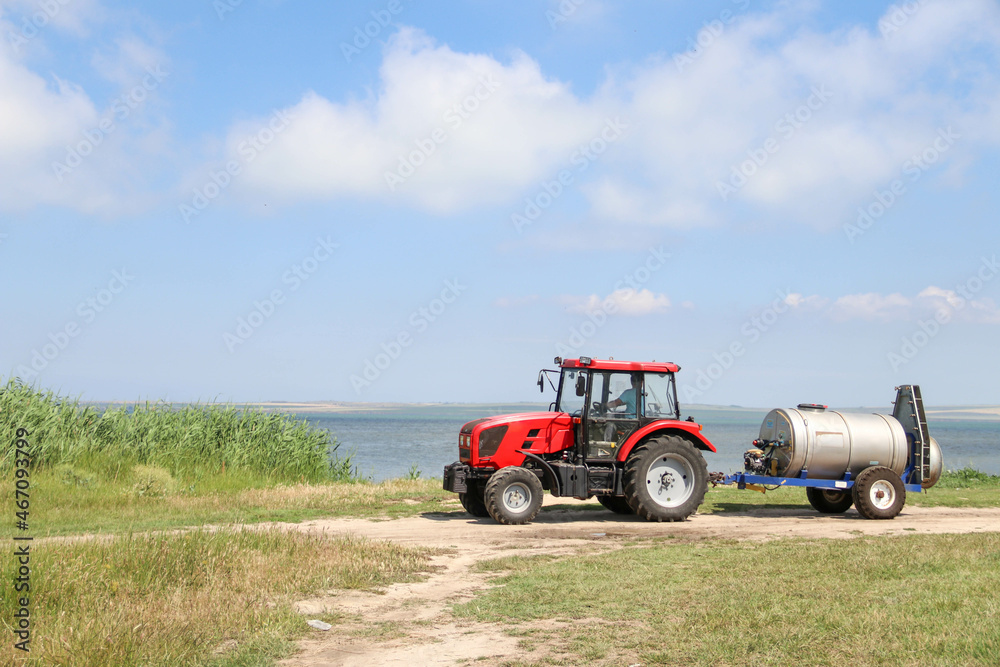 A farmer drives a tractor with a sprayer attached along the bay and reeds. Agriculture A farmer drives a tractor with a sprayer attached along the bay and reeds. Agriculture
