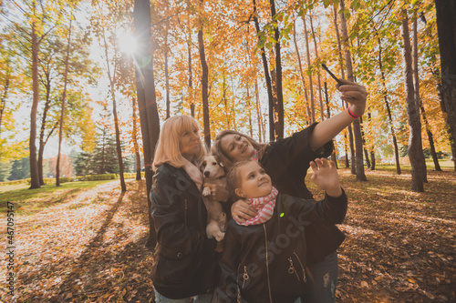 Mother, grandmother and little granddaughter with jack russell terrier dog taking selfie by smartphone outdoors in autumn nature. Family, pets and generation concept