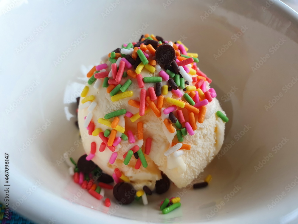 Homemade ice cream one scoop of vanilla is placed in a white cup and sprinkled with rainbow jimmies and chocolate rounds.
Homemade ice cream one scoop of vanilla is placed in a white cup and sprinkled with rainbow jimmies and chocolate rounds.