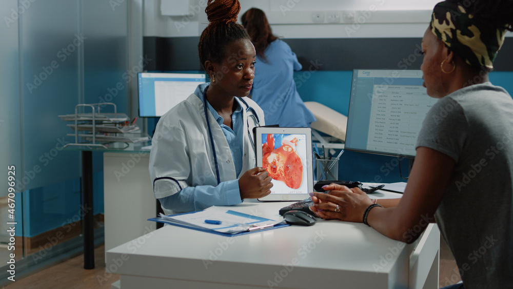 Doctor showing tablet with heart figure for cardiology checkup to patient at consultation. Young parent looking at device with organ for cardiovascular and blood flow healthcare. Doctor showing tablet with heart figure for cardiology checkup to patient at consultation. Young parent looking at device with organ for cardiovascular and blood flow healthcare.