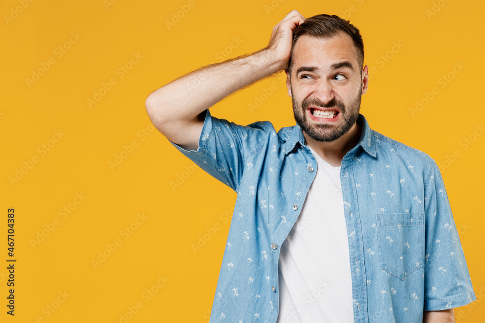 Young puzzled embarrassed bewildered caucasian man 20s wearing blue shirt white t-shirt scratch head look aside say oops isolated on plain yellow background studio portrait. People lifestyle concept. - obrazy, fototapety, plakaty 