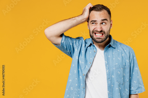 Young puzzled embarrassed bewildered caucasian man 20s wearing blue shirt white t-shirt scratch head look aside say oops isolated on plain yellow background studio portrait. People lifestyle concept. photo