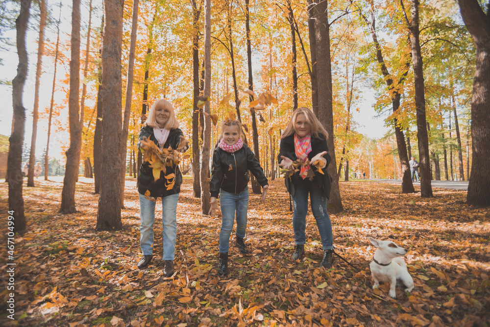 Grandmother and mother with granddaughter throw up fall leaves in autumn park and having fun. Generation, leisure and family concept. Grandmother and mother with granddaughter throw up fall leaves in autumn park and having fun. Generation, leisure and family concept.