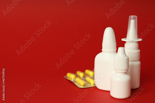 Blank bottles of nasal spray and pills on red background