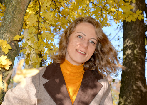 Portrait of a woman in a coat against a background of yellow autumn foliage