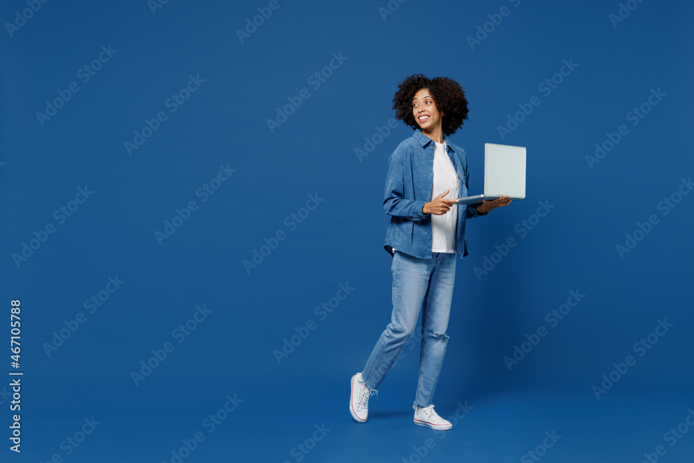 Full body young smiling happy black woman in casual clothes shirt white t-shirt hold use work on laptop pc computer look aside isolated on plain dark blue background studio. People lifestyle concept. Full body young smiling happy black woman in casual clothes shirt white t-shirt hold use work on laptop pc computer look aside isolated on plain dark blue background studio. People lifestyle concept.