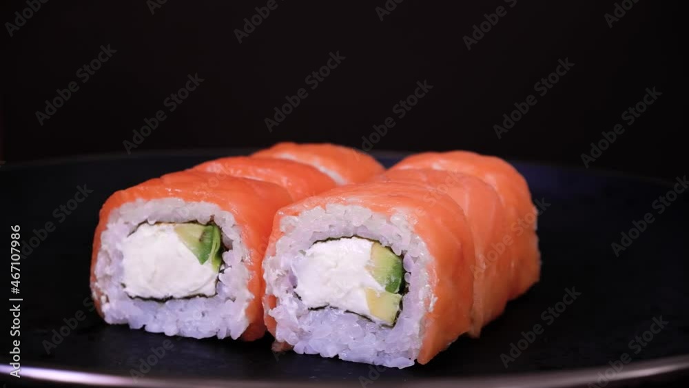 Philadelphia rolls with salmon fish, avocado and cheese spin on a black plate on dark background. Minimal concept Philadelphia rolls with salmon fish, avocado and cheese spin on a black plate on dark background. Minimal concept