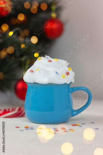 blue cup with drink decorated with whipped cream on table near festive christmas tree