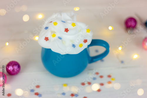 blue cup with a drink decorated with whipped cream and decorative stars on a white table next to christmas balls
