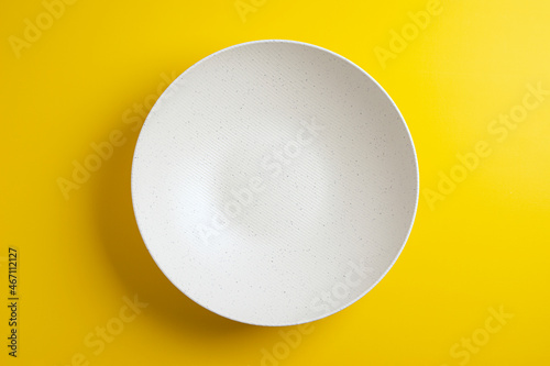 Top down minimalist view of a white bowl on yellow background. White round plate on yellow background