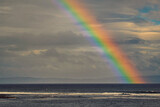 Colorful rainbow over rough dark ocean surface. Dramatic clouds. Waves rushing. Stunning nature landscape.
