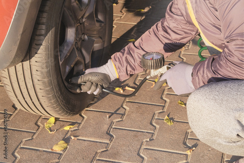 Car service. Male hand in gloves checks pressure in car tires in sunny day. Auto maintenance concept.
