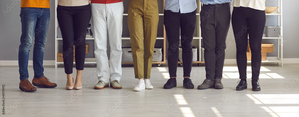 Banner with team of young and senior people who work together standing in company office. Group of friends or colleagues standing in row. Cropped shot of human legs in classic and casual denim pants - obrazy, fototapety, plakaty 